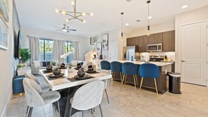 Una cocina moderna con una isla central, taburetes de bar y un área de comedor con una mesa y sillas blancas.