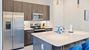 Una cocina moderna con electrodomésticos de acero inoxidable, una isla central e iluminación colgante.