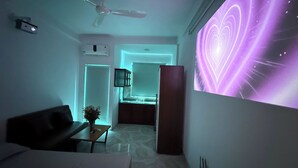 Un salon moderne avec un ventilateur de plafond, un téléviseur à écran plat affichant un motif en forme de cœur, et un coin cuisine en arrière-plan.