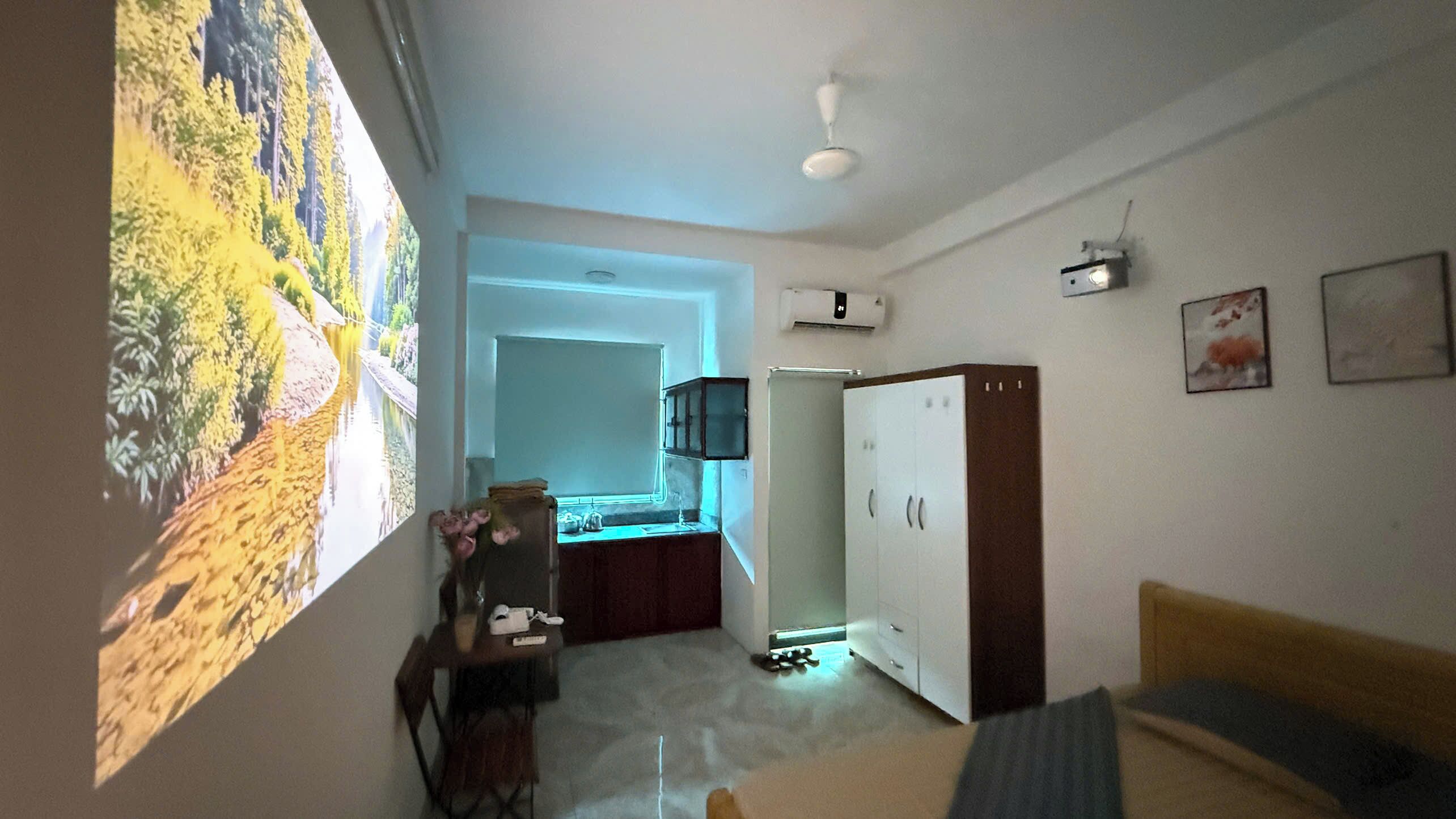 A room with a bed, a desk with a chair, a wardrobe, and a large window with a view of trees.