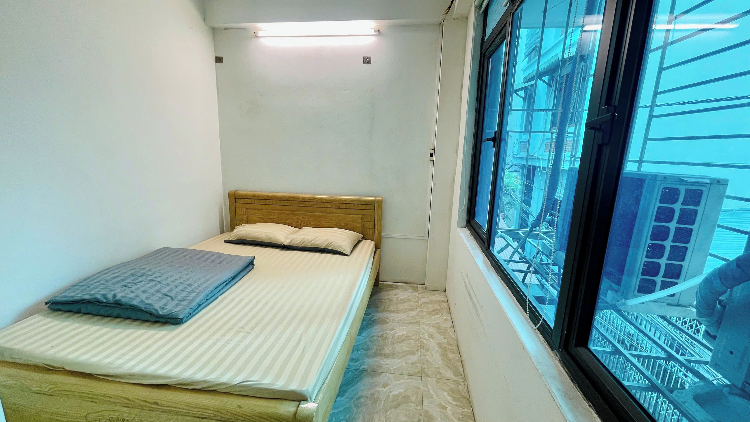 Una habitación pequeña y estrecha con una cama individual, una ventana y vista a un edificio.