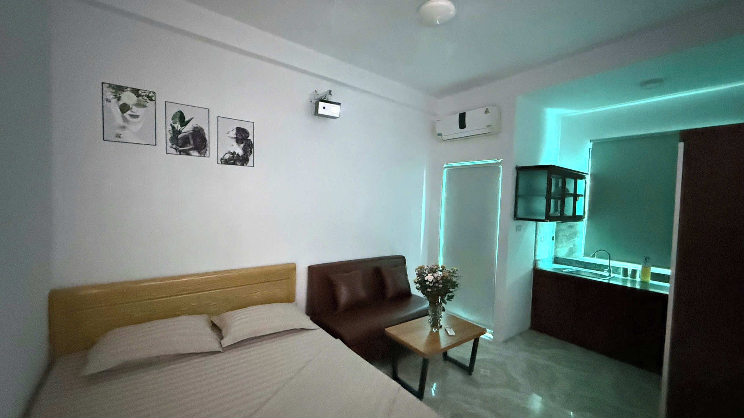 Une chambre d’hôtel avec un lit, un canapé marron, une petite table avec un vase et un miroir.