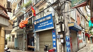 Une rue étroite, bordée de bâtiments des deux côtés, un magasin fermé avec une enseigne bleue, et un scooter garé devant.