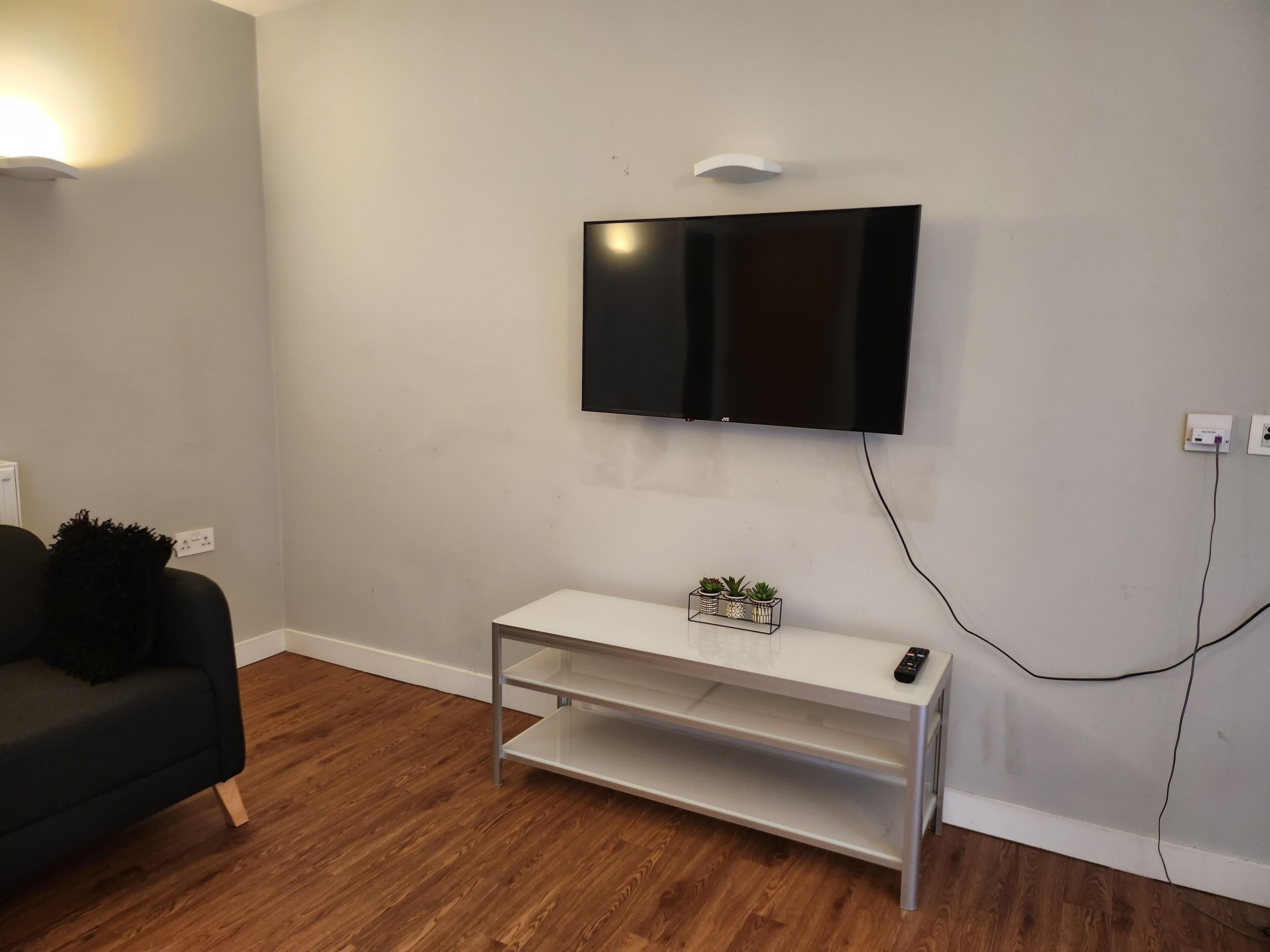 A modern living room with a flat-screen TV mounted on the wall, a white console table with plants, and a black sofa.