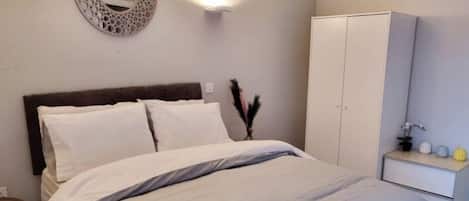 A bedroom with a bed, a wardrobe, a bedside table, and a wall-mounted mirror.