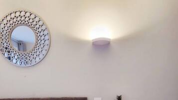 Un dormitorio con una cama, un espejo redondo, una lámpara de pared y una pequeña mesa con un florero.