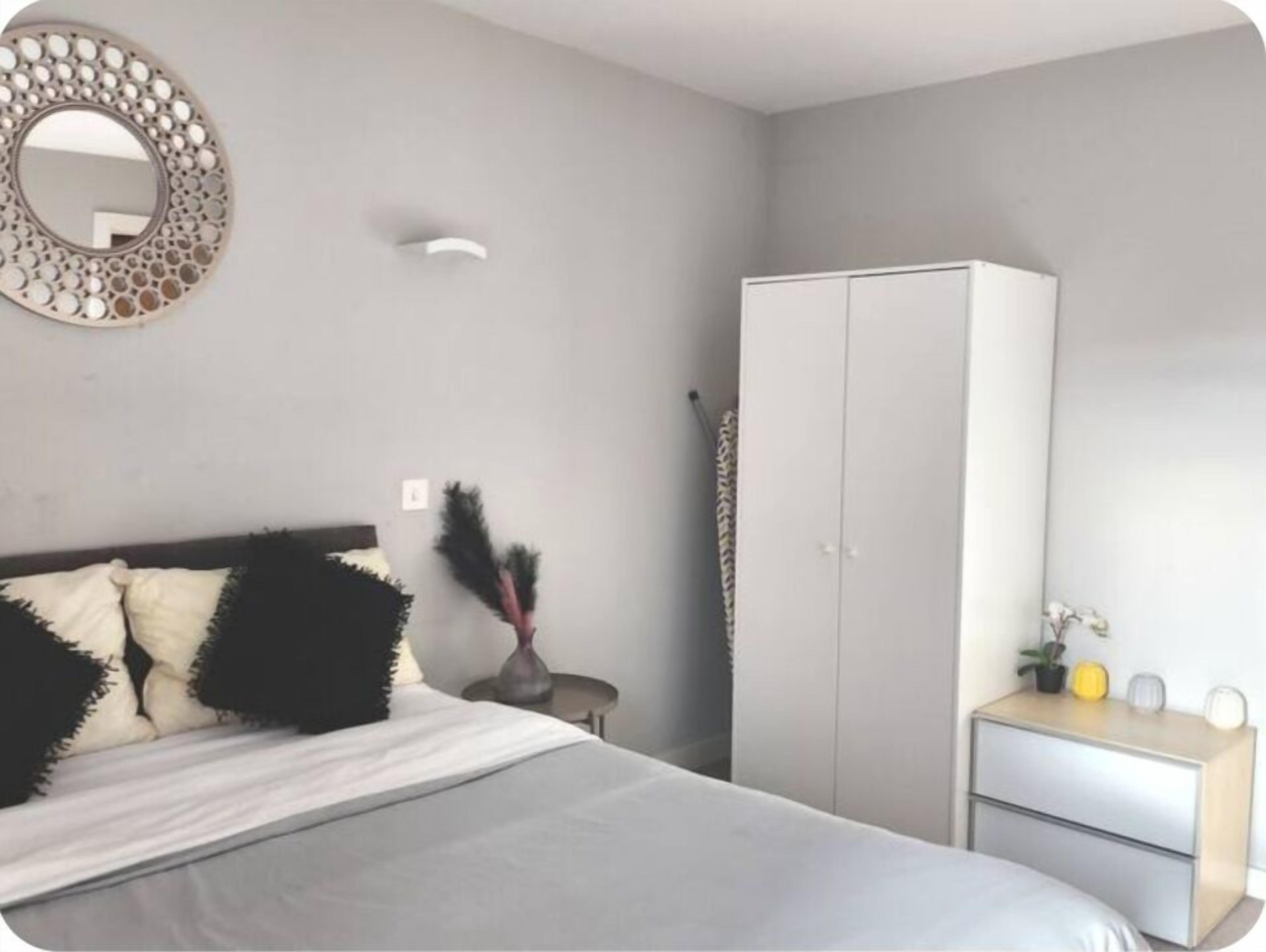 A bedroom with a bed, a wardrobe, a mirror, and a bedside table with a lamp.