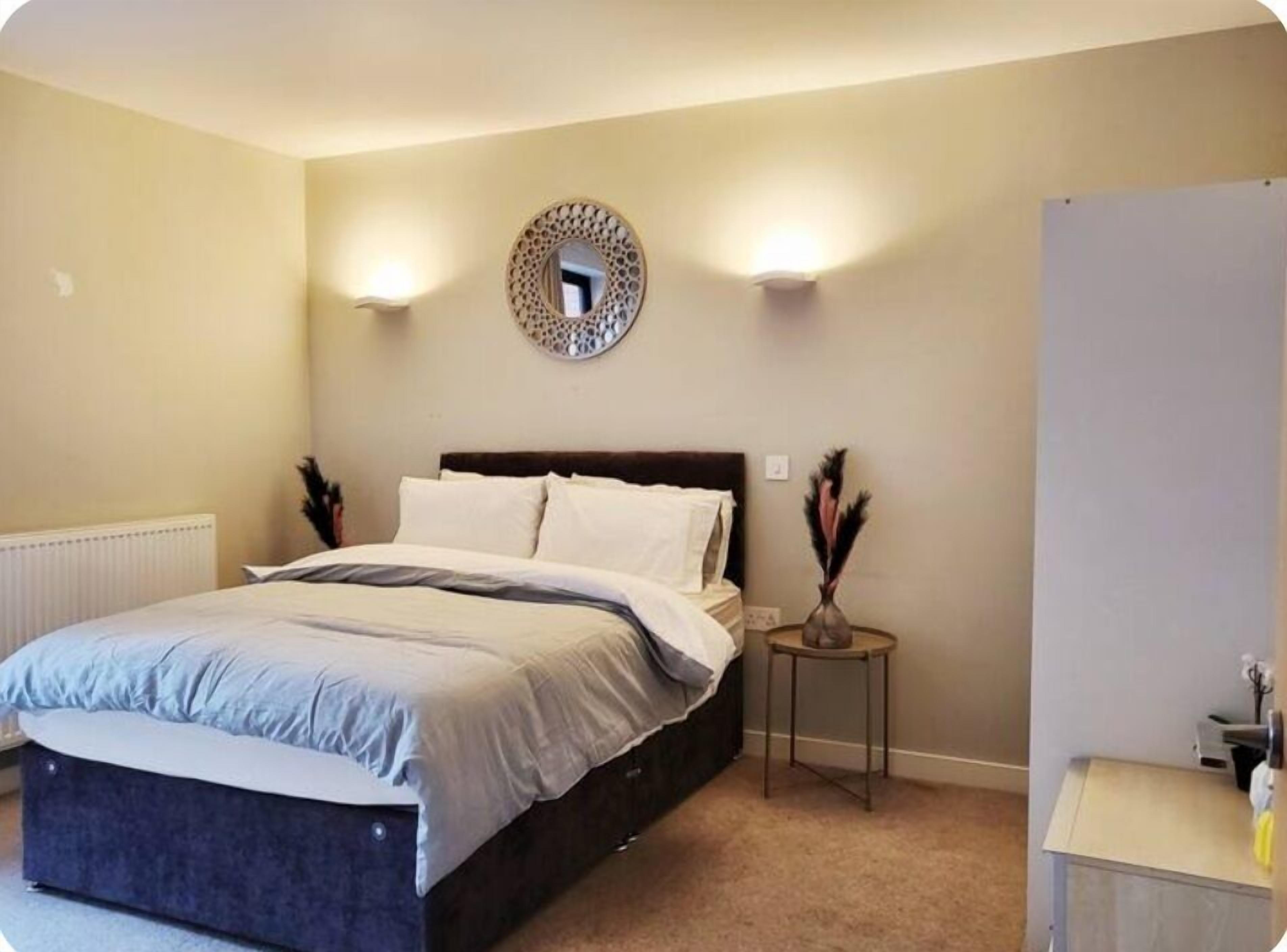 A bedroom with a bed, bedside lamps, a round mirror, and a small table with decorative items.