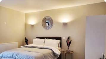 A bedroom with a bed, bedside lamps, a round mirror, and a small table with decorative items.