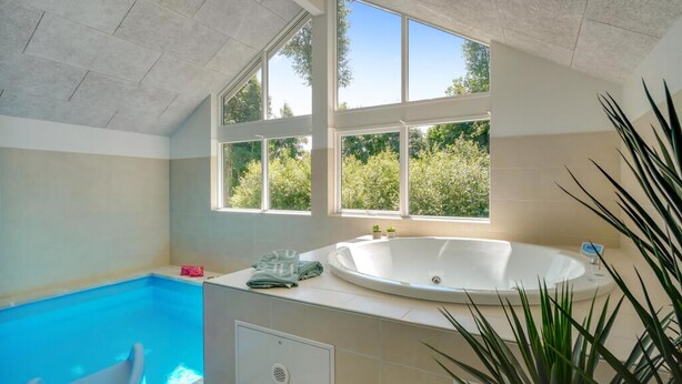 A bathroom with a bathtub, a window, and a view of greenery outside.