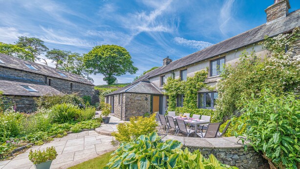 A stone house with a garden patio, outdoor seating, and a large tree.