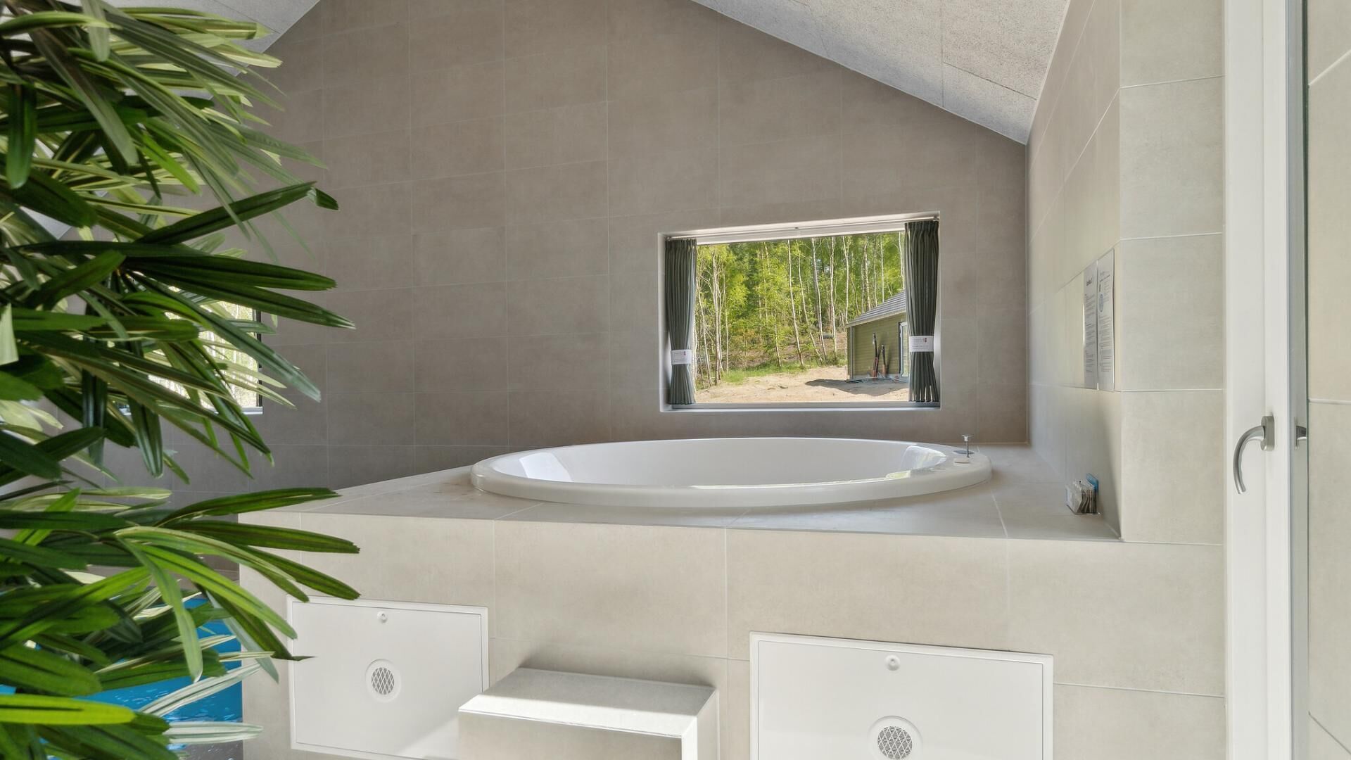 A modern bathroom with a freestanding bathtub, a window with a view of trees, and a shower area.