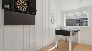 A room with a dartboard, a foosball table, and a window with a view of buildings.