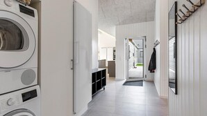 Un lavadero con lavadoras y secadoras apiladas, un armario negro y un pasillo que conduce a una zona de cocina.