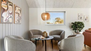 A modern living room with two grey armchairs, a round coffee table, and a wooden pendant light. There are abstract paintings on the wall and a window with a view of trees. - VillaVilla 806 - Fjellerup, Østjylland (Glesborg)