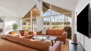 A spacious living room with a large sectional sofa, a coffee table, and a TV mounted on the wall.
