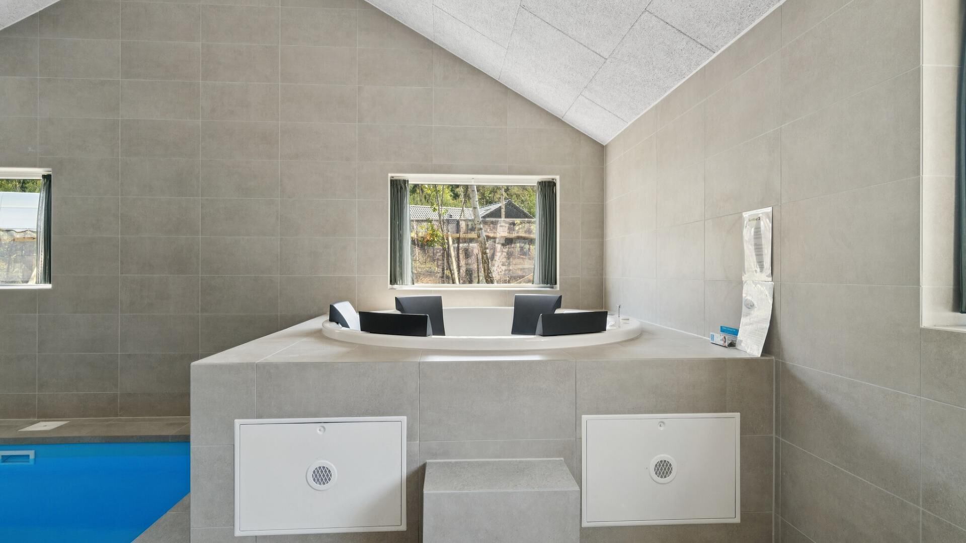 A modern bathroom with a built-in bathtub, a window with a view of a building, and a small pool area.