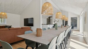 Moderni olohuone, jossa on pitkä ruokapöytä, useita tuoleja, sohva ja roikkuvat, punotut valaisimet.