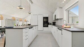 A modern kitchen with white cabinetry, a central island, pendant lighting, and a view of the outdoors through a window. - VillaVilla 807 - Fjellerup, Østjylland (Glesborg)