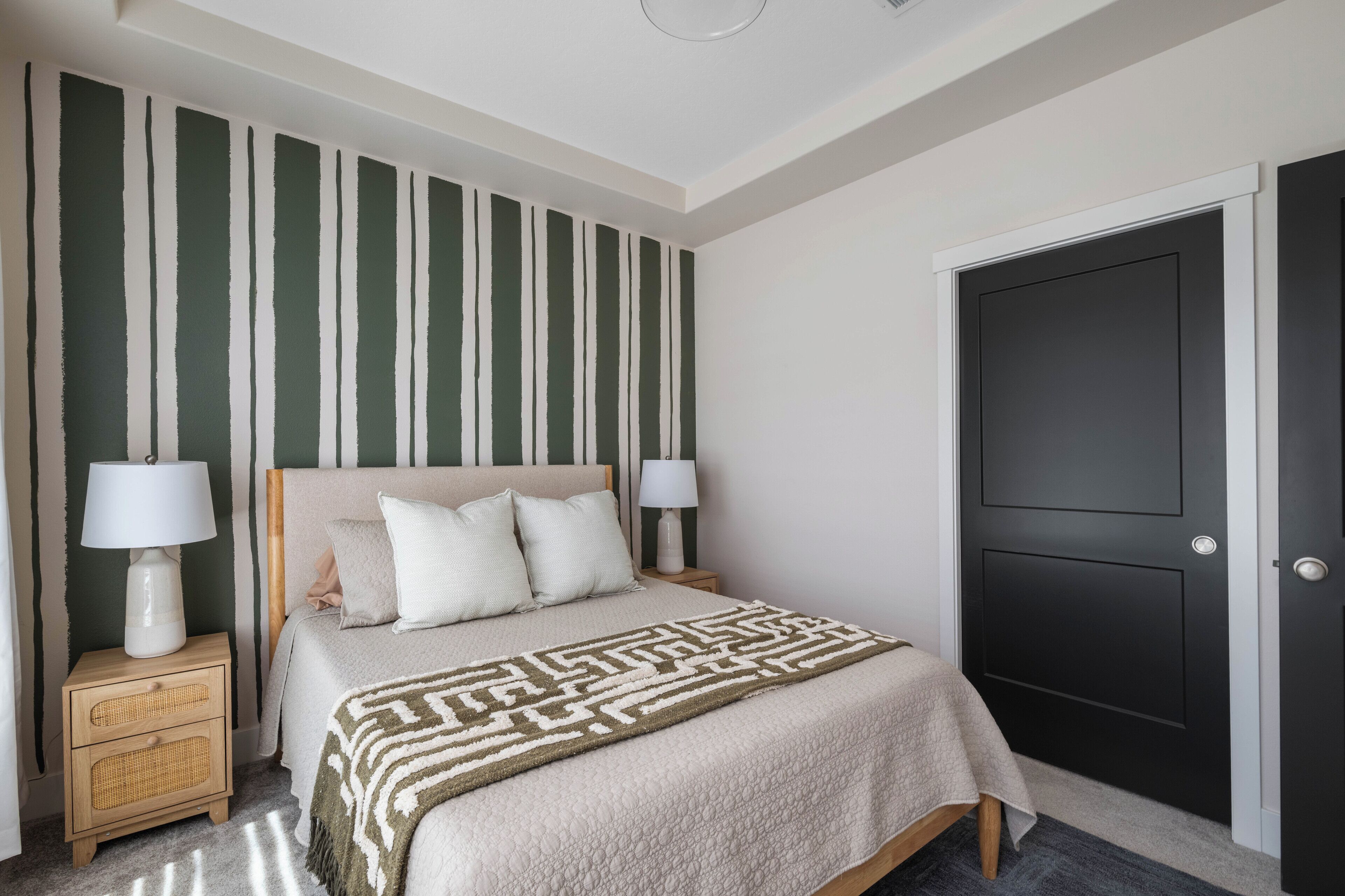 Une chambre à coucher avec un lit, deux tables de chevet avec des lampes, une porte sombre et un mur à rayures verticales.