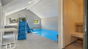 Una piscina interior moderna con un tobogán azul, una sauna y una pequeña mesa con un tendedero.