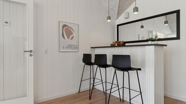 A modern interior with white paneled walls, a black-framed mirror, and three black bar stools.