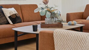 A living room with a brown sofa, a coffee table, a vase with a flower, a knitting ball, and a pair of glasses.