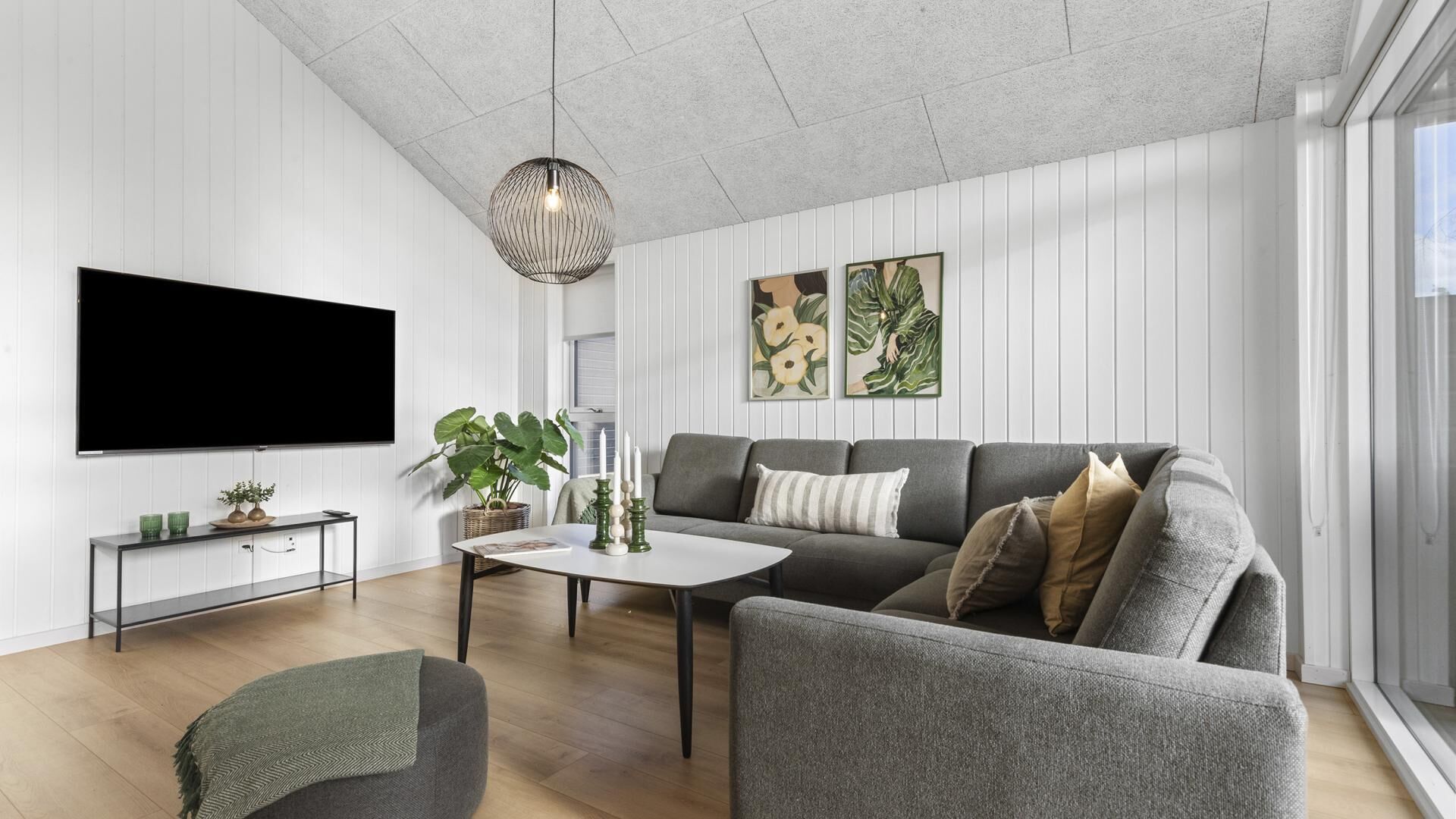 Ein modernes Wohnzimmer mit Flachbildfernseher, grauem Sofa, Couchtisch und einer hängenden Pendelleuchte.