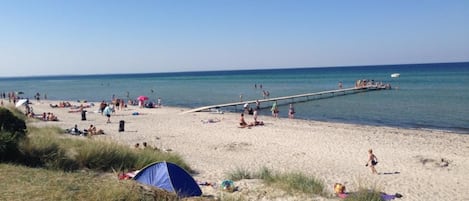 A beach with people, a pier, and a tent.