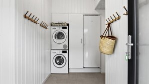 A laundry room with stacked washers and dryers, a refrigerator, and a hanging basket.