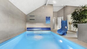 An indoor swimming pool with a blue slide, tiled walls, and a potted plant.