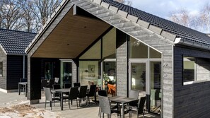 A modern building with a sloped roof, large glass windows, and outdoor seating area with tables and chairs. - VillaVilla 810 - Fjellerup, Østjylland (Glesborg)