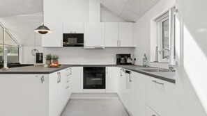 A modern kitchen with white cabinets, a built-in oven, a coffee maker, and a window with a view.