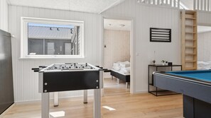 Une pièce équipée d’un baby-foot, d’une table de billard et d’une fenêtre donnant sur un immeuble.