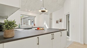 Uma cozinha moderna com bancada escura, armários brancos e uma luminária pendente.