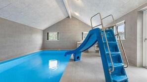 Ein Hallenbad mit einer blauen Rutsche, einer Leiter und zwei Fenstern.
