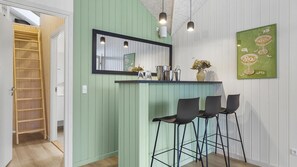 Eine Küche mit grüner Wand, einem spiegelnden Schwarzrahmen, einer Bar mit Hockern und einem Kunstwerk in grünem Rahmen.