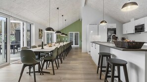 Une cuisine moderne avec des meubles blancs, un coin repas doté d’une longue table et un bar avec des tabourets.