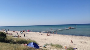 Ein Strand mit einem Steg, der sich ins Wasser erstreckt, Zelten und Menschen.