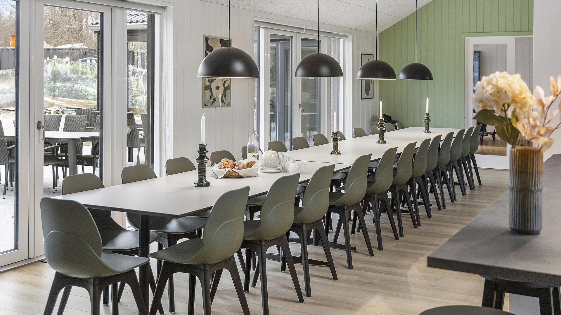 A long dining table with chairs, pendant lights, and a vase with flowers.