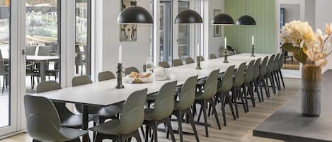 A long dining table with chairs, pendant lights, and a vase with flowers.
