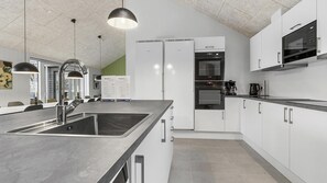 Eine moderne Küche mit Edelstahlgeräten, einer großen Kochinsel mit Spüle, Pendelleuchten und Blick auf den Essbereich.