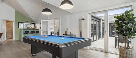A pool table in a room with a wooden floor, a hanging light fixture, and a sliding glass door leading outside.