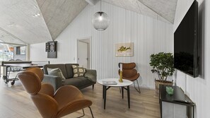 Un salon moderne avec une table de ping-pong, des fauteuils en cuir, une table ronde avec un livre, un téléviseur fixé au mur et un luminaire suspendu au plafond.