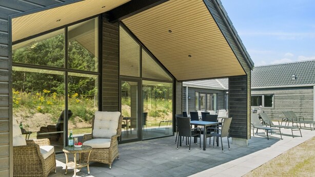 Un patio moderno al aire libre con paredes de vidrio, mobiliario de mimbre y una zona de comedor.