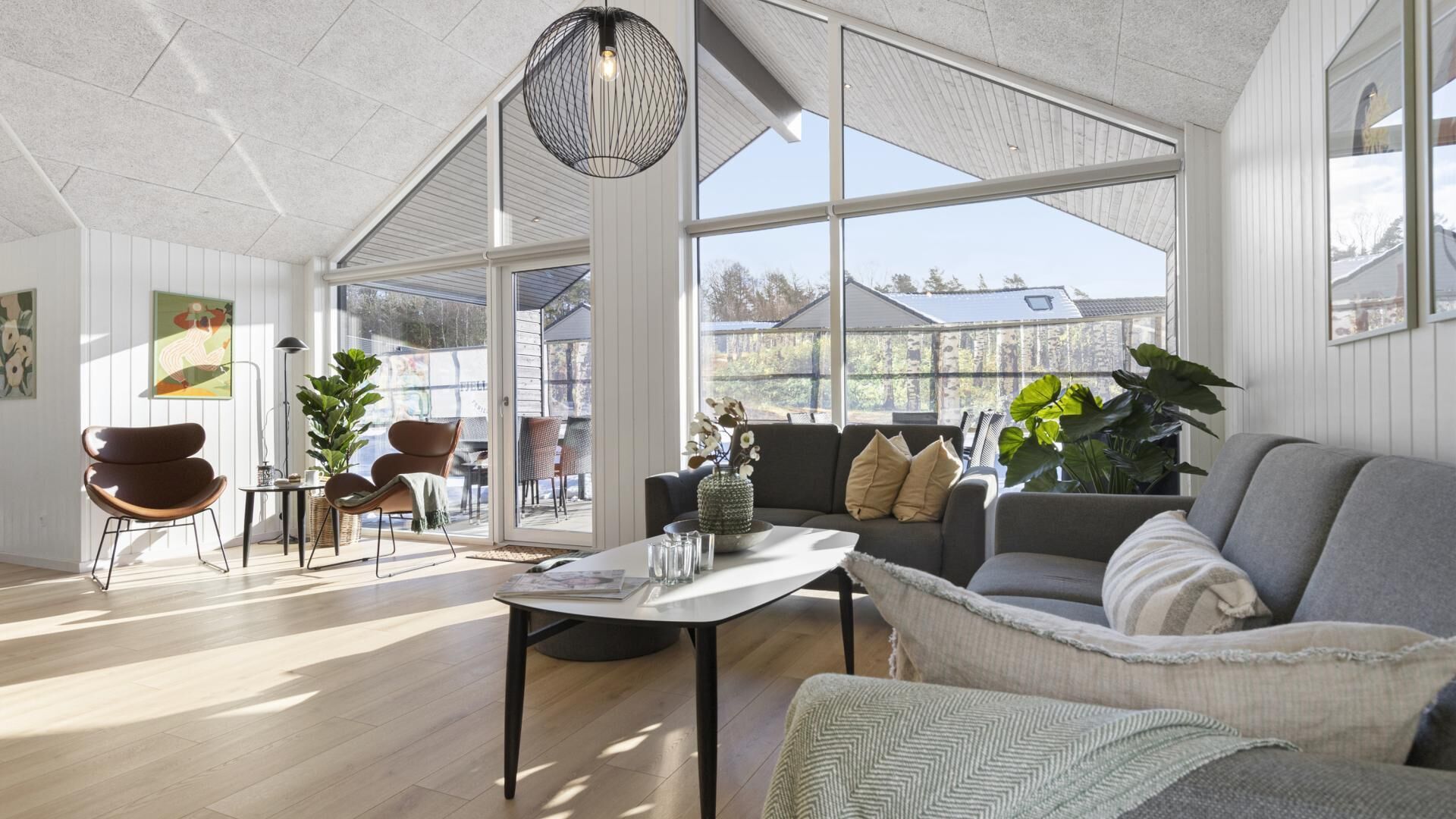 Ein geräumiges Wohnzimmer mit großem Fenster, einer modernen Chandelierleuchtre und einer Mischung an Möbeln, darunter ein Sofa, Sessel und ein Couchtisch.