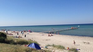 Een strand met een pier die zich in het water uitstrekt, mensen ontspannen op het zand en een tent op het strand.