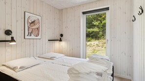Makuuhuoneessa on kaksi sänkyä, kehystetty taideteos, seinälle asennetut valaisimet ja liukuoven kautta avautuva näkymä vehreään maisemaan.