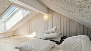 Une chambre avec un plafond en pente, des murs en bois, un puits de lumière et un lit recouvert de linge de lit blanc.
