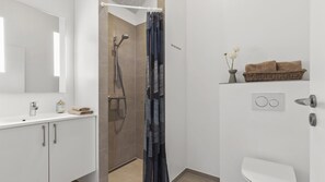 Ein modernes Badezimmer mit Dusche, Toilette, Waschbecken und Spiegel.